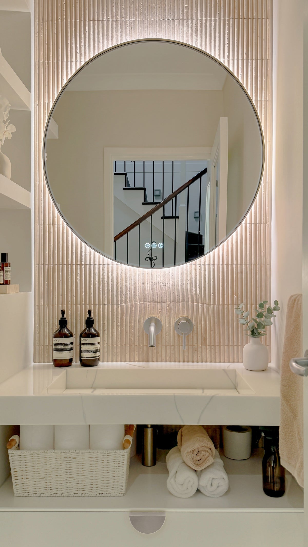 The Capri round 800 mm framed backlit LED mirror in Brushed Nickel, above a white stone basin with a matching Milano wall spout and mixer, fluted travertine wall