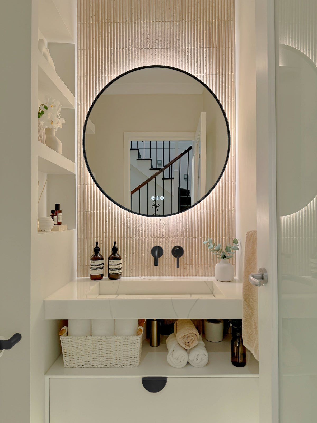 The Capri round 800 mm framed backlit LED mirror in Matte Black, in a powder room above a floating white vanity with matching hardware