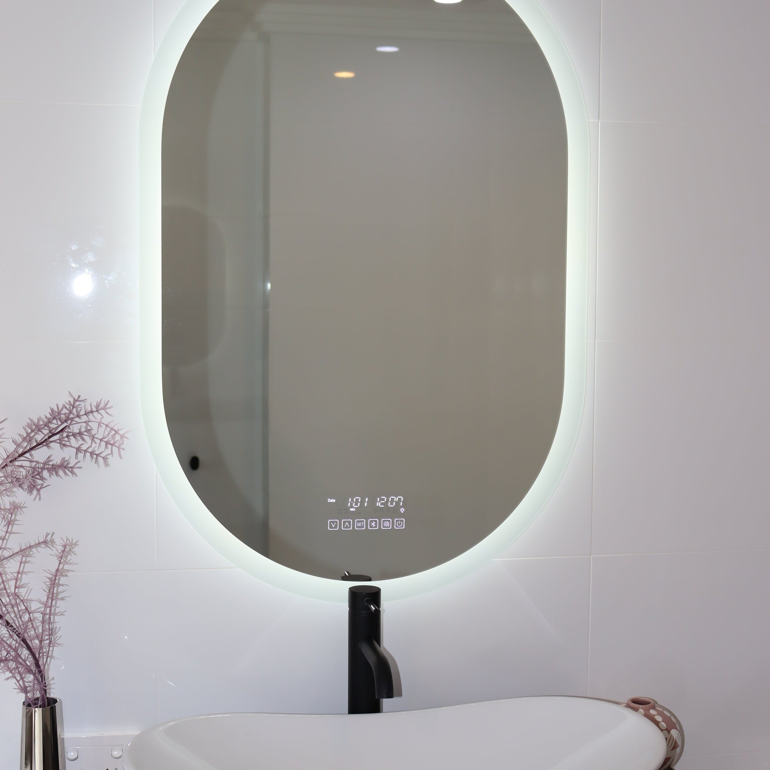 Oval Smart LED mirror above black countertop and white vessel sink