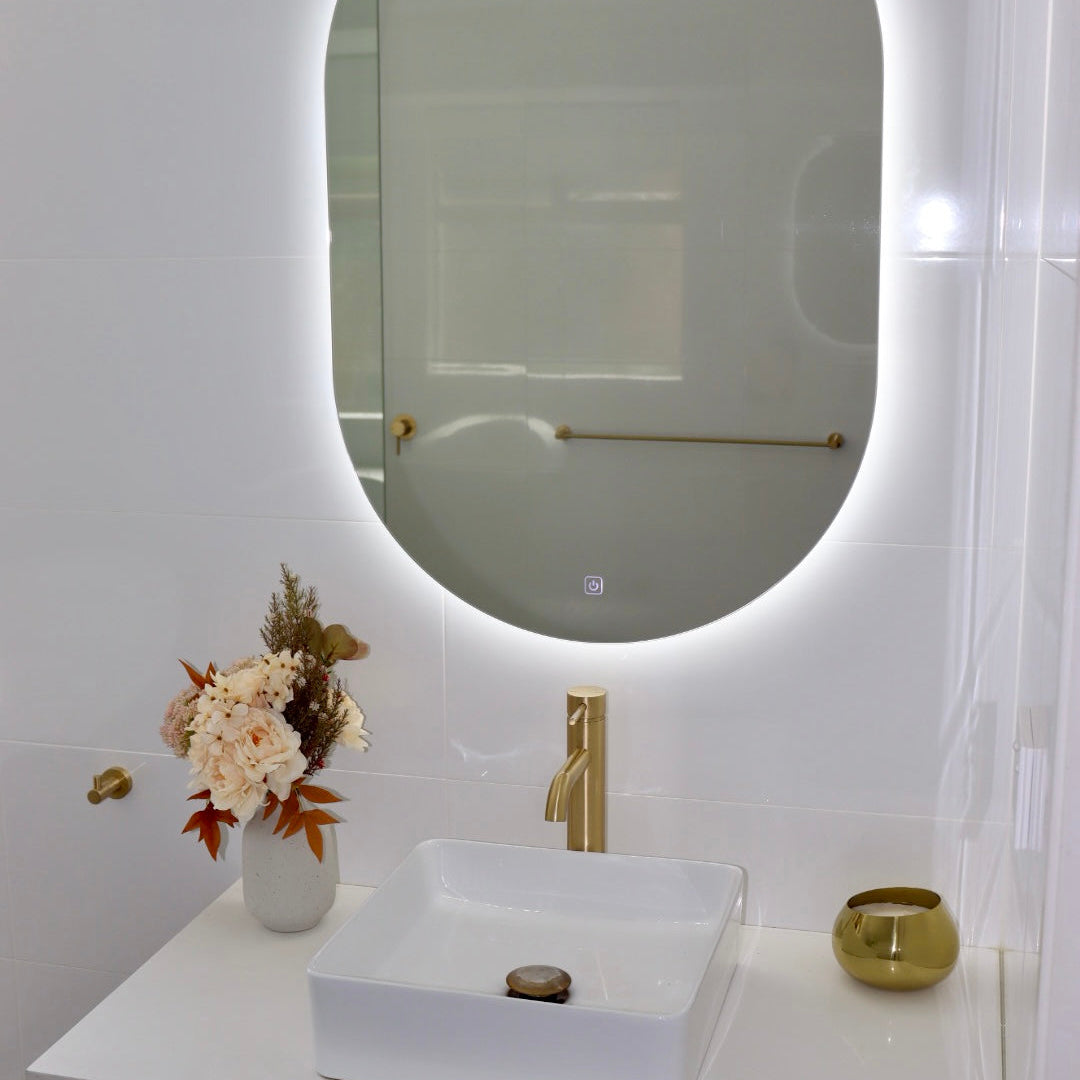 Compact Vanity Area with Oval LED Mirror Above Brown and White Cabinet in Shiny White Tiled Bathroom