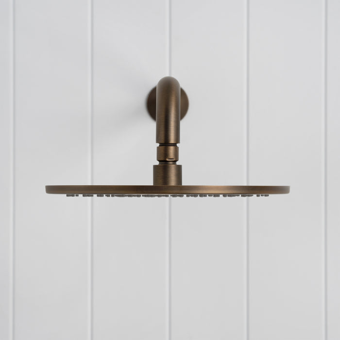 Bordeaux Wall Mounted Shower Head with Arm in Antique Brass, front view on a white vertical-panelled wall