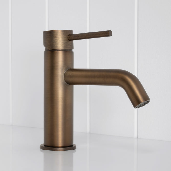 Vienna Short Basin Mixer in Antique Brass, side profile of the curved spout and pin lever, white vertical-panelled wall