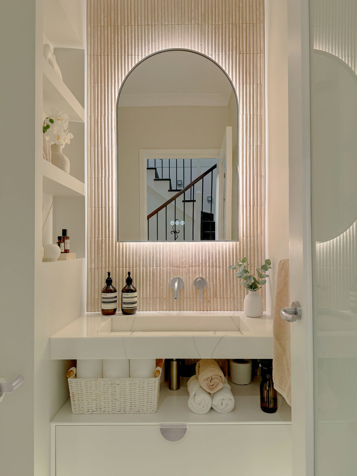 The Marbella 600 x 1000 mm arch framed backlit LED mirror in Brushed Nickel, in a powder room above a floating white vanity with matching hardware