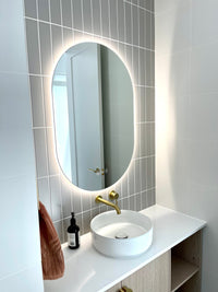 Neutral-Themed Powder Room with Well-lit Smart LED Mirror, Gold Faucet, White Sink, Wooden Cabinet