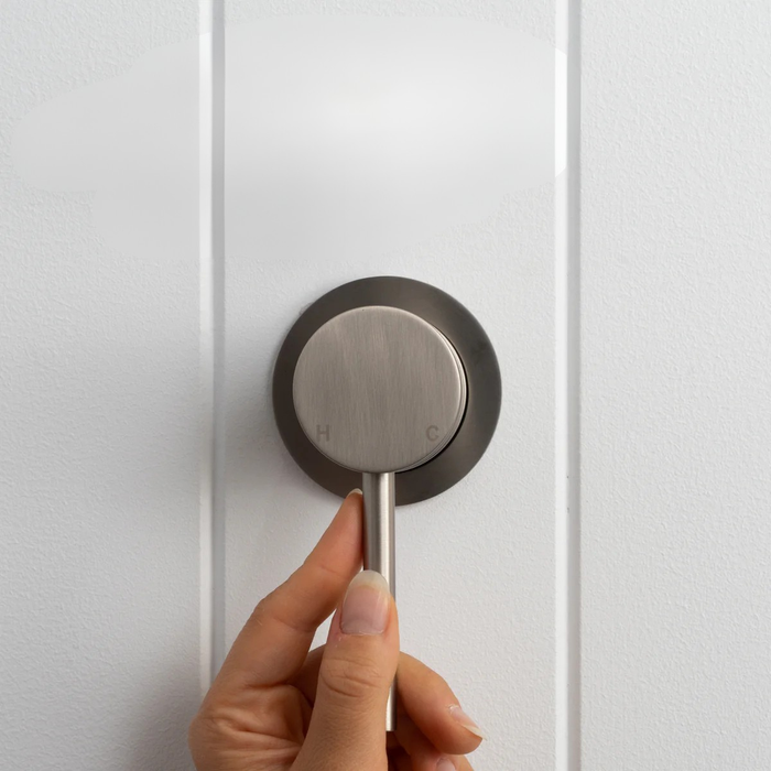 Milano Wall Mixer in Brushed Nickel, hand on the pin lever, front view on a white vertical-panelled wall