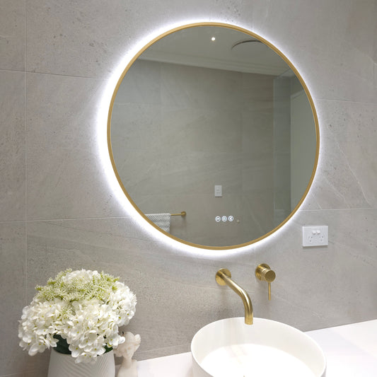 Bellagio round LED mirror with a gold frame switched to cool white light above a round basin with brushed brass tapware