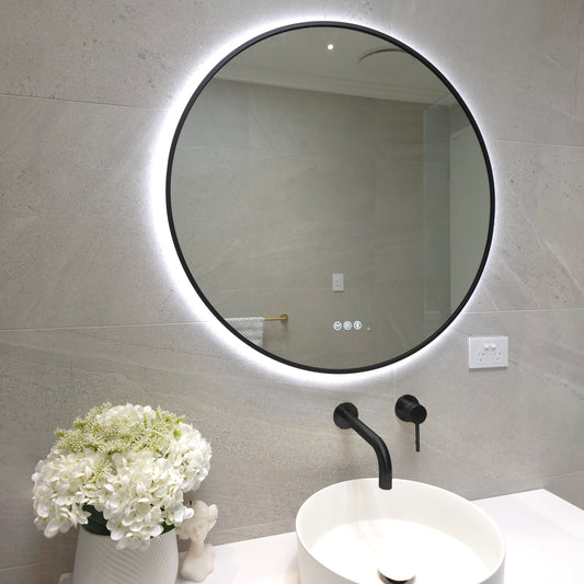 Bellagio round LED mirror with a matte black frame switched to cool white light above a vessel basin
