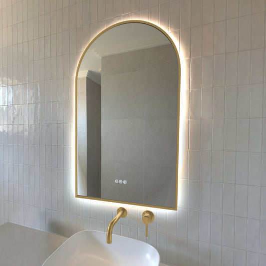 Calais arch-shaped backlit LED mirror with a gold wrap-around frame above a vessel basin with brushed brass tapware