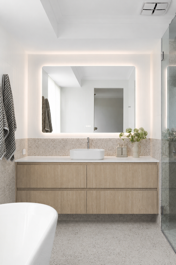 The Florence backlit LED bathroom mirror above a timber vanity with white vessel basin and freestanding bath
