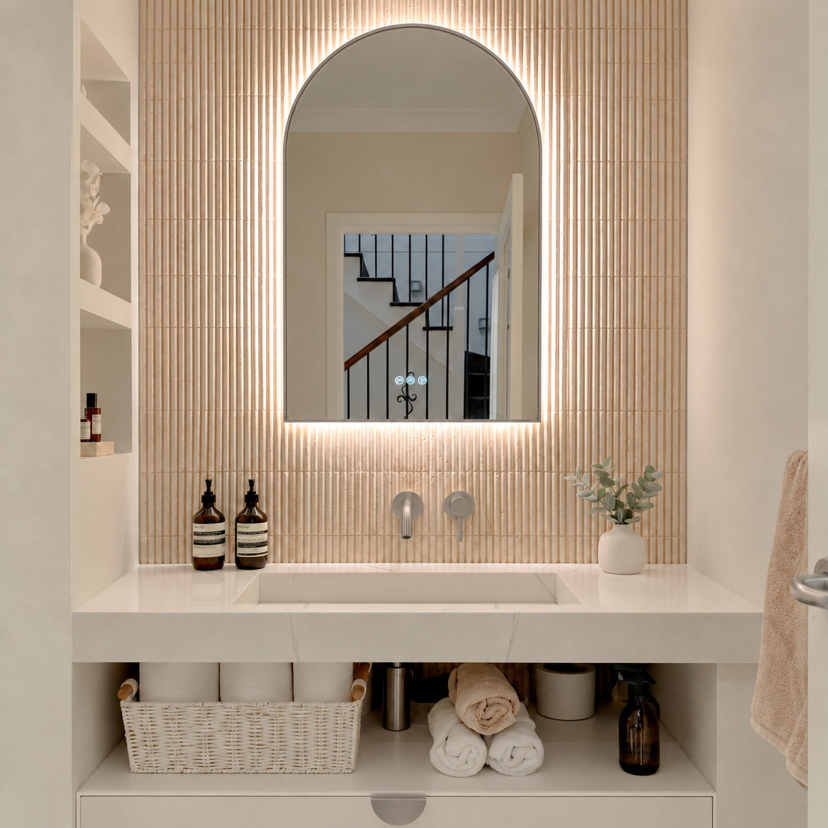 The Marbella 600 x 1000 mm arch framed backlit LED mirror in Brushed Nickel, lit and seen straight-on above a white stone basin with a matching wall spout and mixer