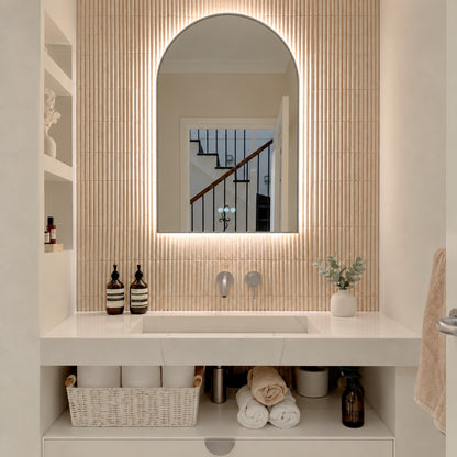 The Marbella 600 x 1000 mm arch framed backlit LED mirror in Brushed Nickel, lit and seen straight-on above a white stone basin with a matching wall spout and mixer