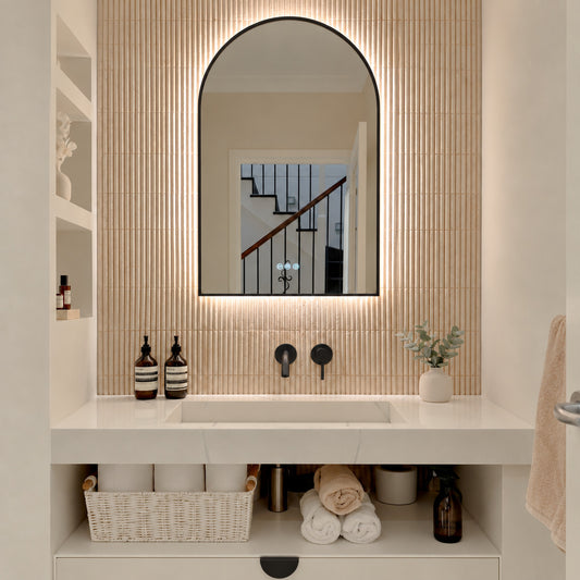 The Marbella 600 x 1000 mm arch framed backlit LED mirror in Matte Black, lit and seen straight-on above a white stone basin with a matching wall spout and mixer