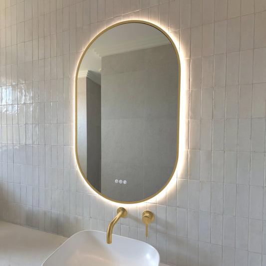 Marseille pill-shaped backlit LED mirror with a gold wrap-around frame above a vessel basin with brushed brass tapware