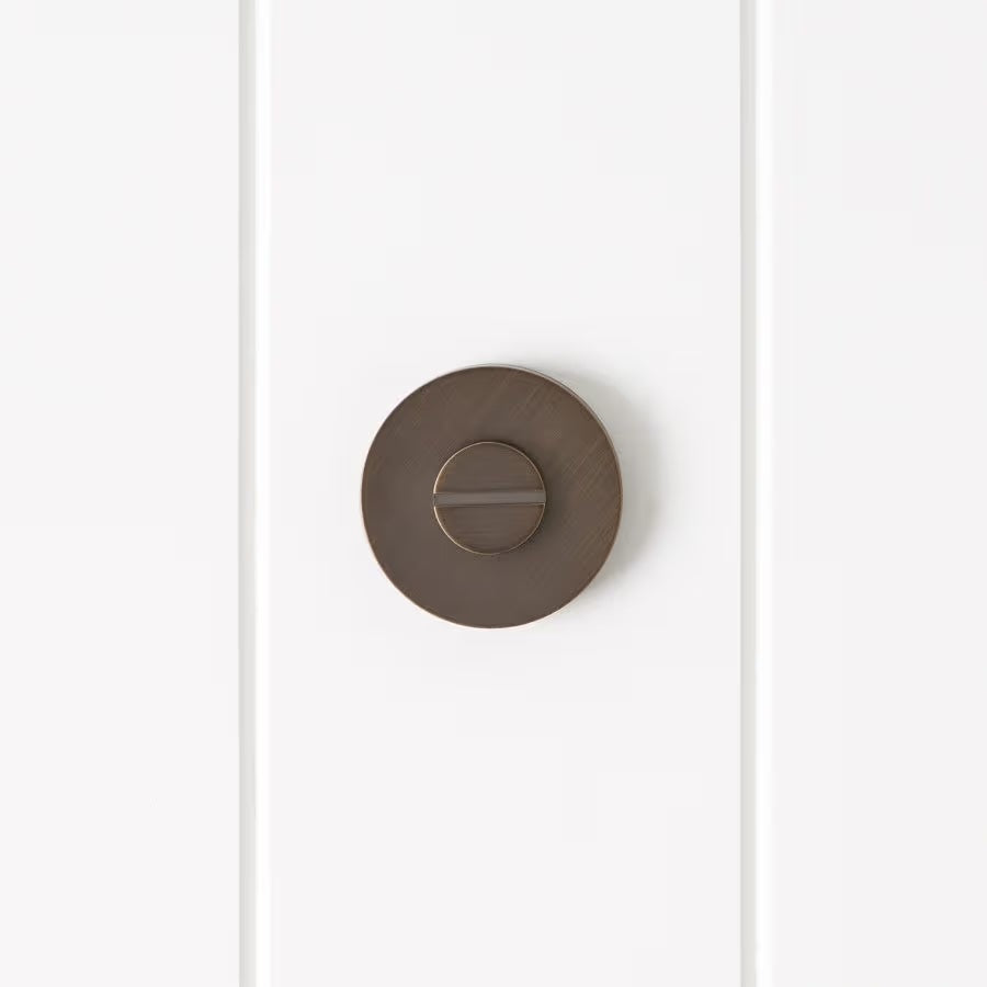 Prague Door Lock in Antique Brass, front view of the slotted emergency release on a white vertical-panelled wall
