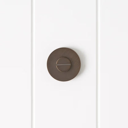 Prague Door Lock in Antique Brass, front view of the slotted emergency release on a white vertical-panelled wall