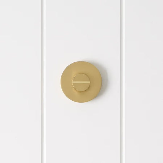 Prague Door Lock in Brushed Brass, front view of the slotted emergency release on a white vertical-panelled wall