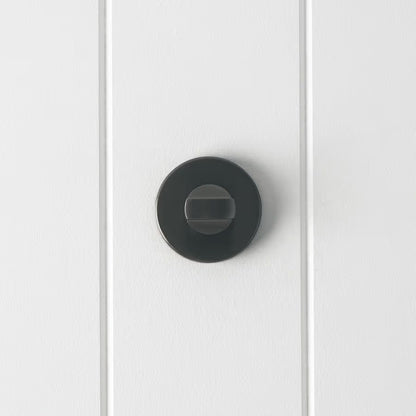 Prague Door Lock in Brushed Gunmetal, front view of the thumb-turn on its round rose, white vertical-panelled wall