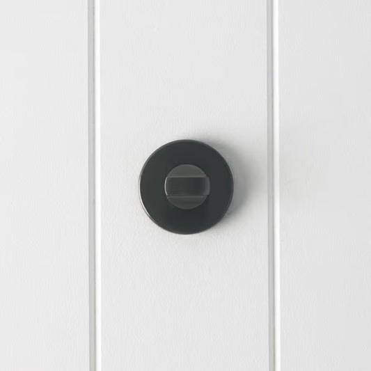 Prague Door Lock in Brushed Gunmetal, front view of the thumb-turn on its round rose, white vertical-panelled wall