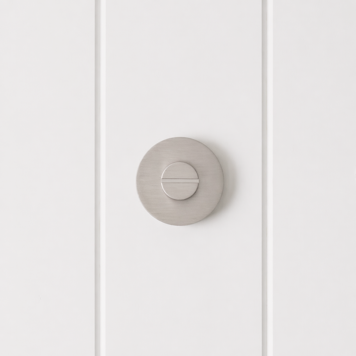 Prague Door Lock in Brushed Nickel, front view of the slotted emergency release on a white vertical-panelled wall