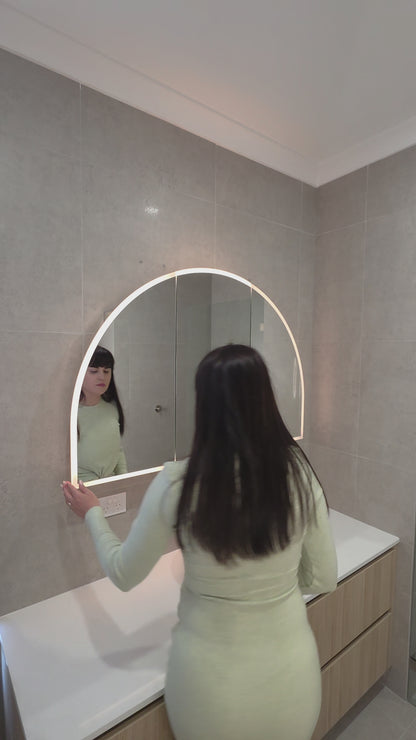 Female opening the door of an LED arched mirror cabinet showing adjustable glass internal shelves