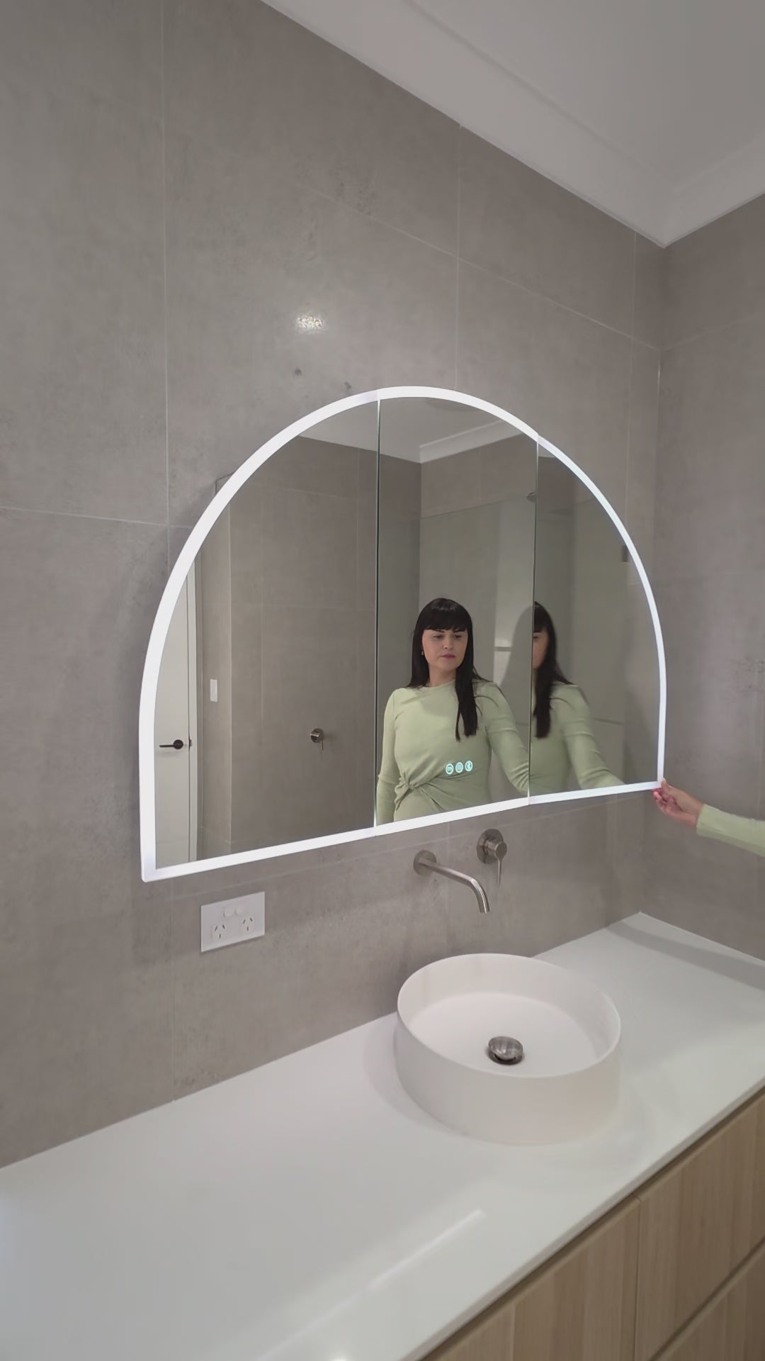 Female opening the door of an LED arched mirror cabinet and touching the display buttons