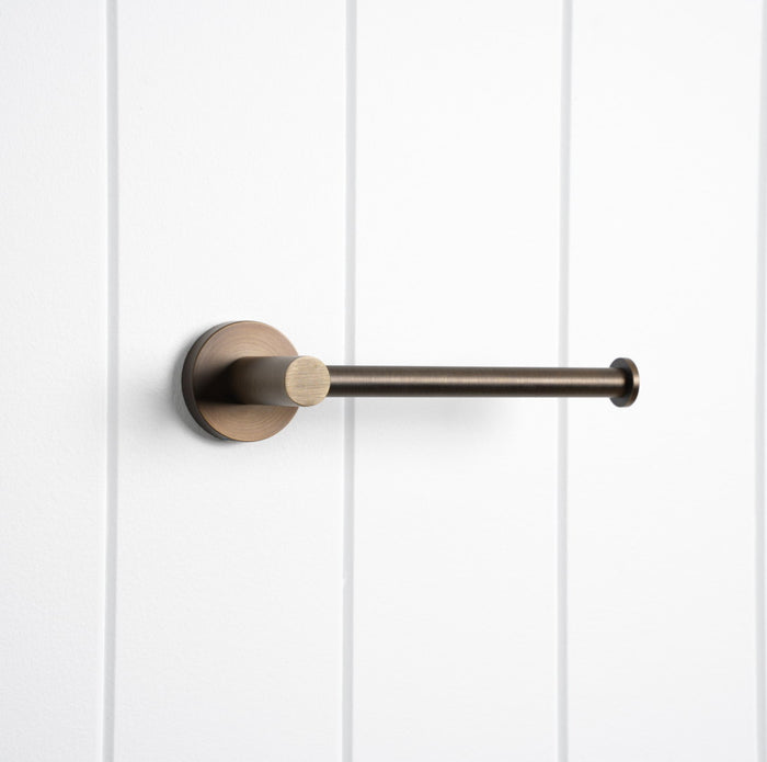 Lille Toilet Roll Holder in Antique Brass, three-quarter view, empty, on a white vertical-panelled wall