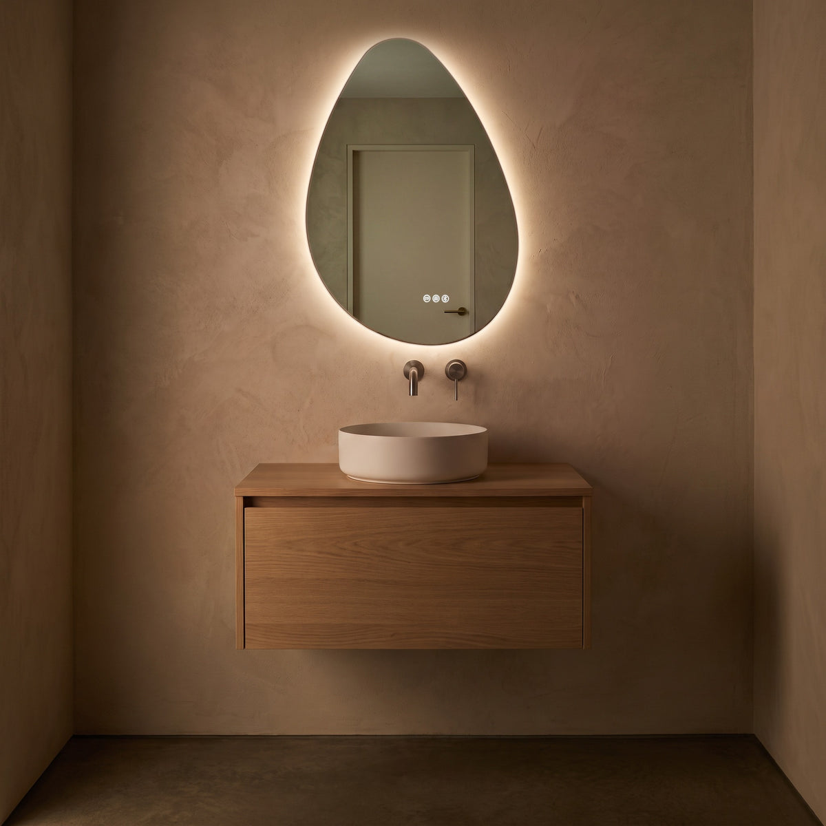 The Sorrento frameless backlit LED mirror hung portrait, glowing in a dim evening powder room above an oak vanity