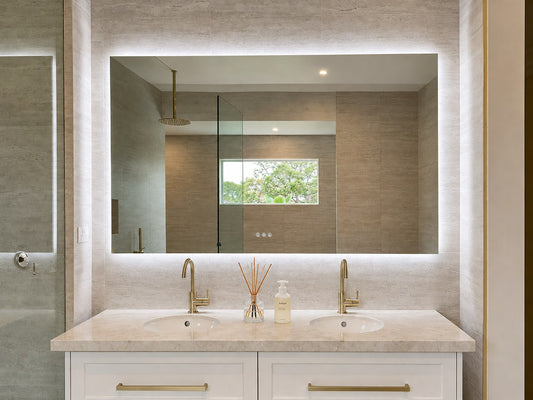 The Venice backlit LED bathroom mirror above a white double vanity with brass tapware and stone benchtop