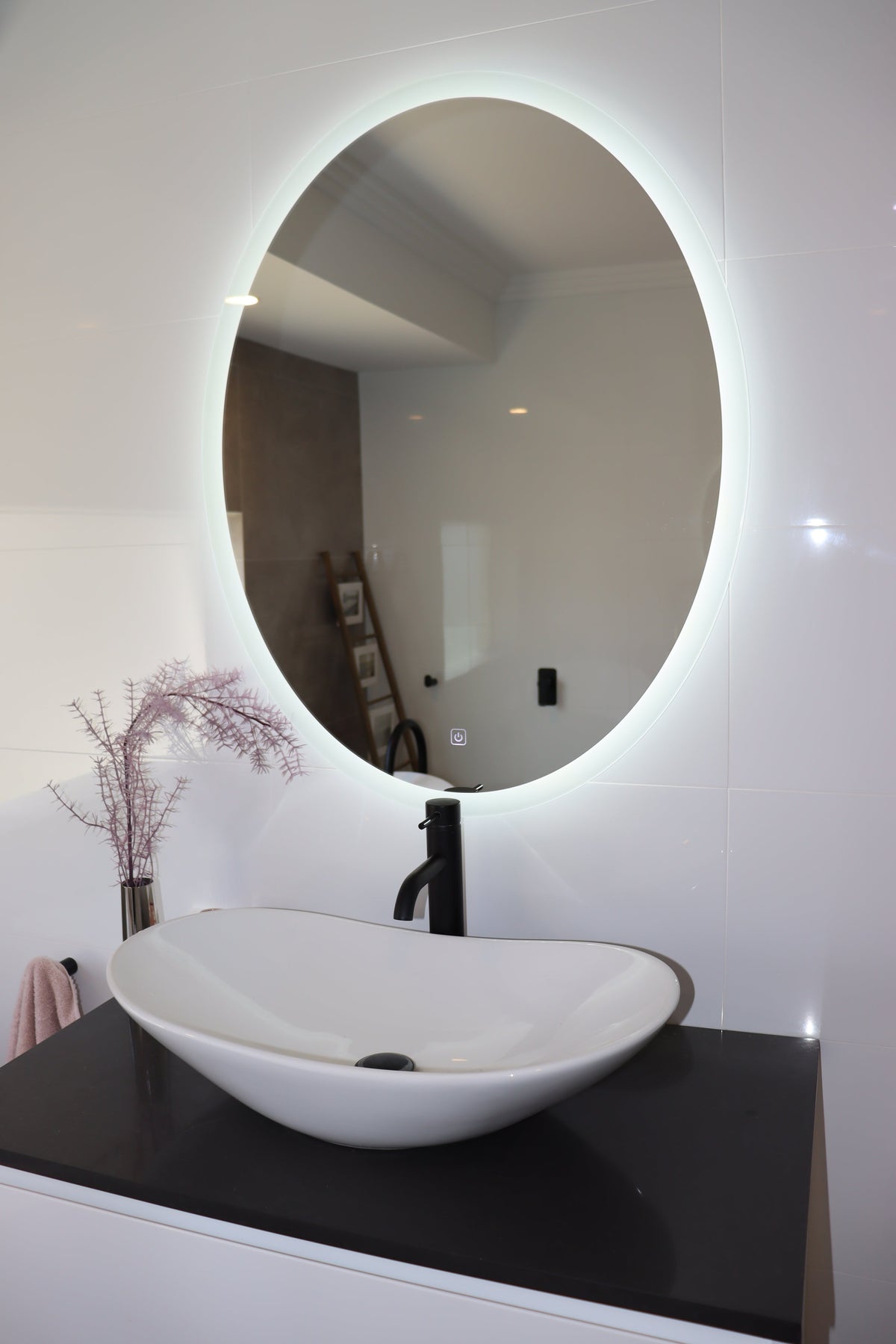 Oval LED Mirror above White Glossy Bathroom with White Vessel Sink and Contrasting Black Countertop