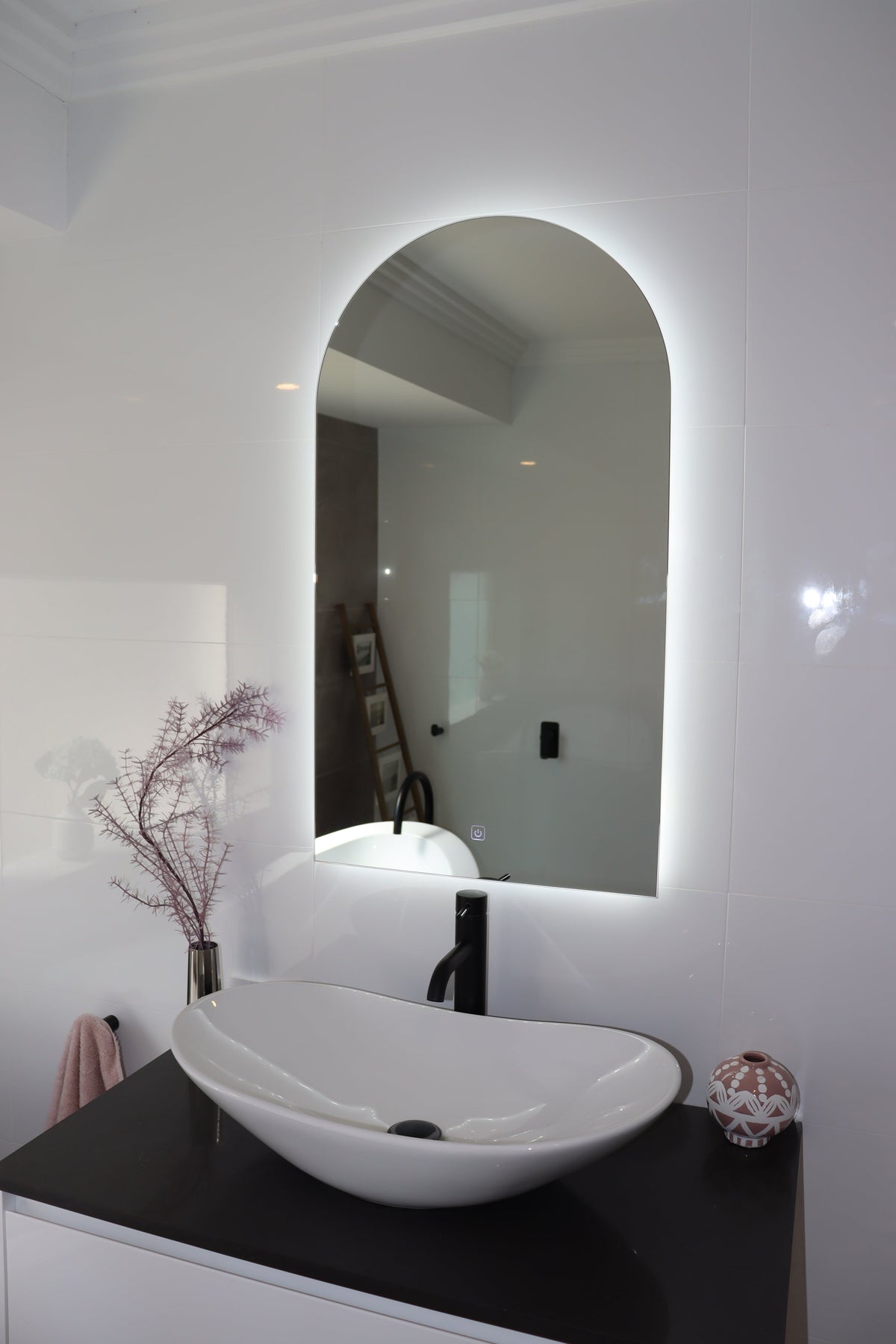 Elegant Curved LED Mirror Illuminating White Shiny Tiles and Black Countertop with White Vessel Sink