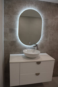 Left view of vanity space with Oval LED mirror emitting light, white floating cabinet with gold accents