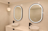 Cream-themed bathroom displaying Dual Oval Smart LED mirrors, white vessel sinks, and pendant light