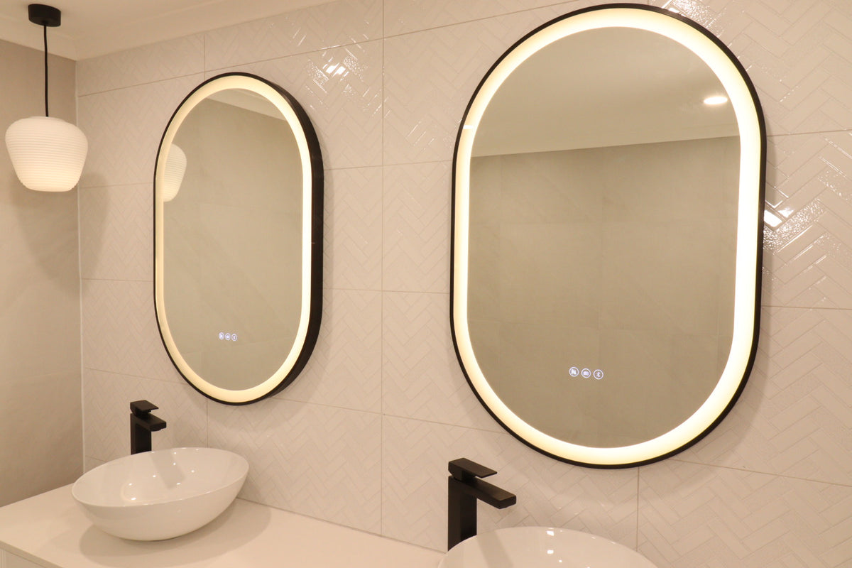 Low angle right side view of two oval Smart LED mirrors in cream-themed bathroom with black accents