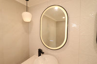 Left Oval Smart LED Mirror with Black Frame in Cream-Themed Powder Room featuring Black Accents