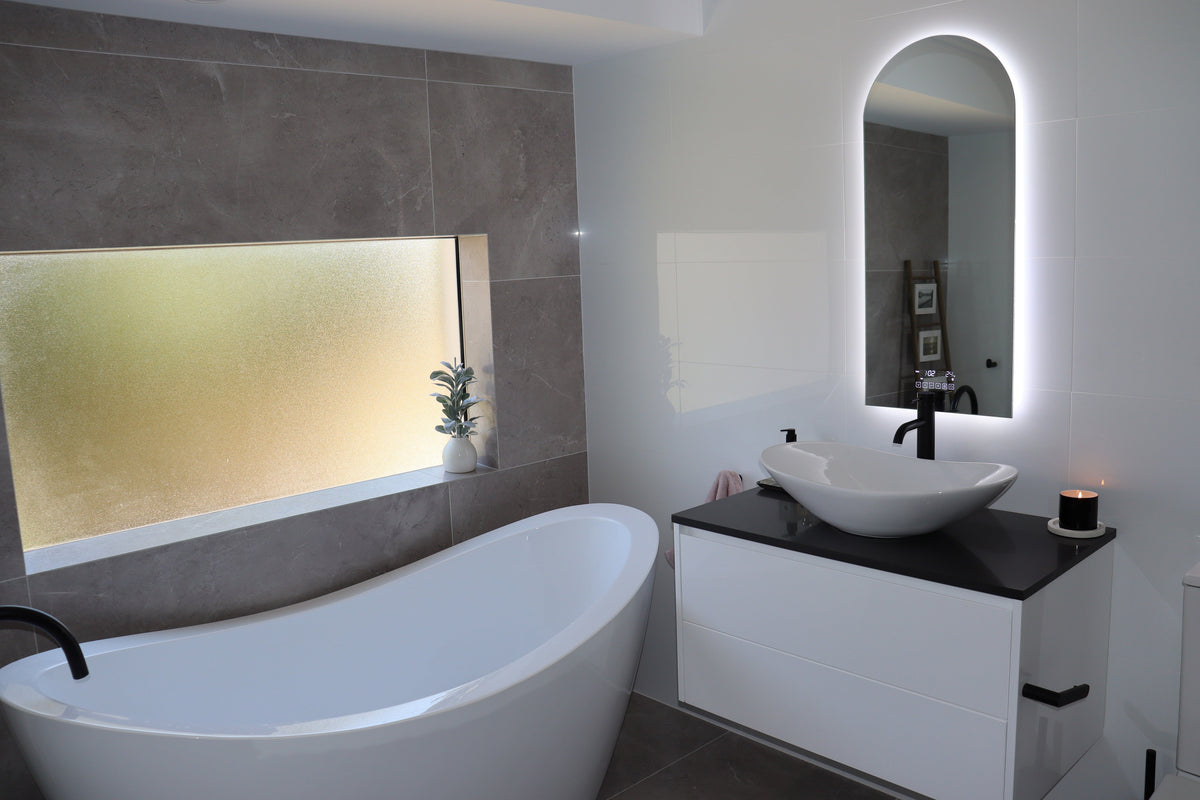 Backlit LED Mirror, White Vanity Cabinet and White Bathtub in White-Grey Bathroom with Black Accents