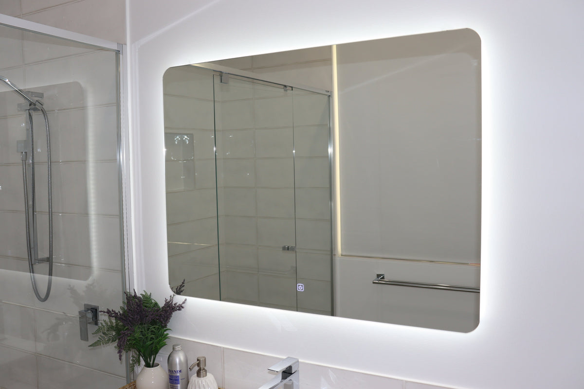 All-white bathroom illuminated by large backlit LED mirror in white light mode with silver accents
