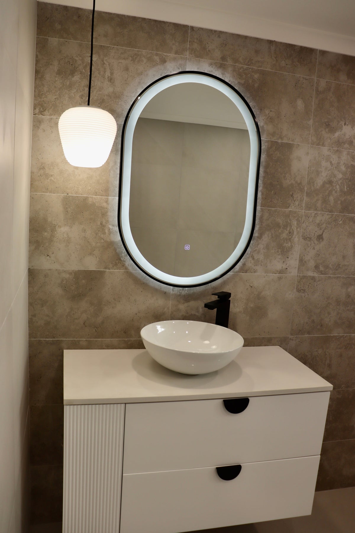 Left Side Shot on Vanity Area with Oval Black Frame LED Mirror, White Vessel Sink, and Pendant Light
