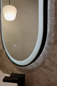 View of Lower Section of Pill-Shaped Black Frame LED Mirror on Grey Wall