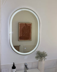 Silver Frame LED Vanity Mirror Reflecting Opposite Wall's Paintings