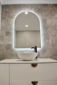 Glowing Backlit LED Mirror on Greyish-Brown Wall with Dirty White Vanity Cabinet and Vessel Sink