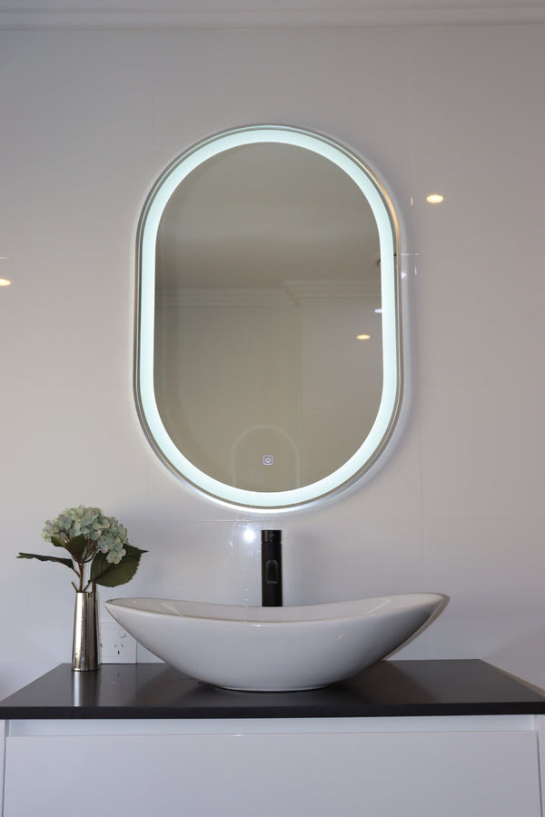 Classy Vanity LED Mirror with White Wall, White Vessel Sink, and Stainless Flower Vase on Black Countertop