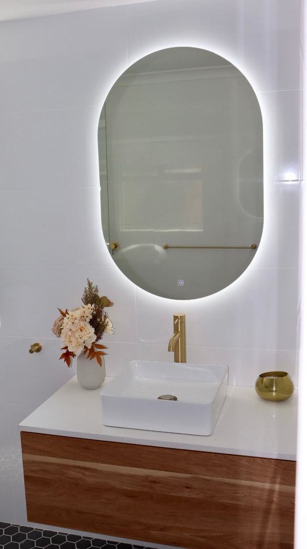 White-Lit LED Mirror Above White-Brown Floating Cabinet with Gold Accents on Shiny White Tiled Wall